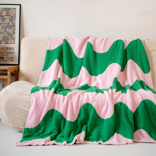 A dual-textured throw with green and pink waves pattern, draped over the back of a sofa.