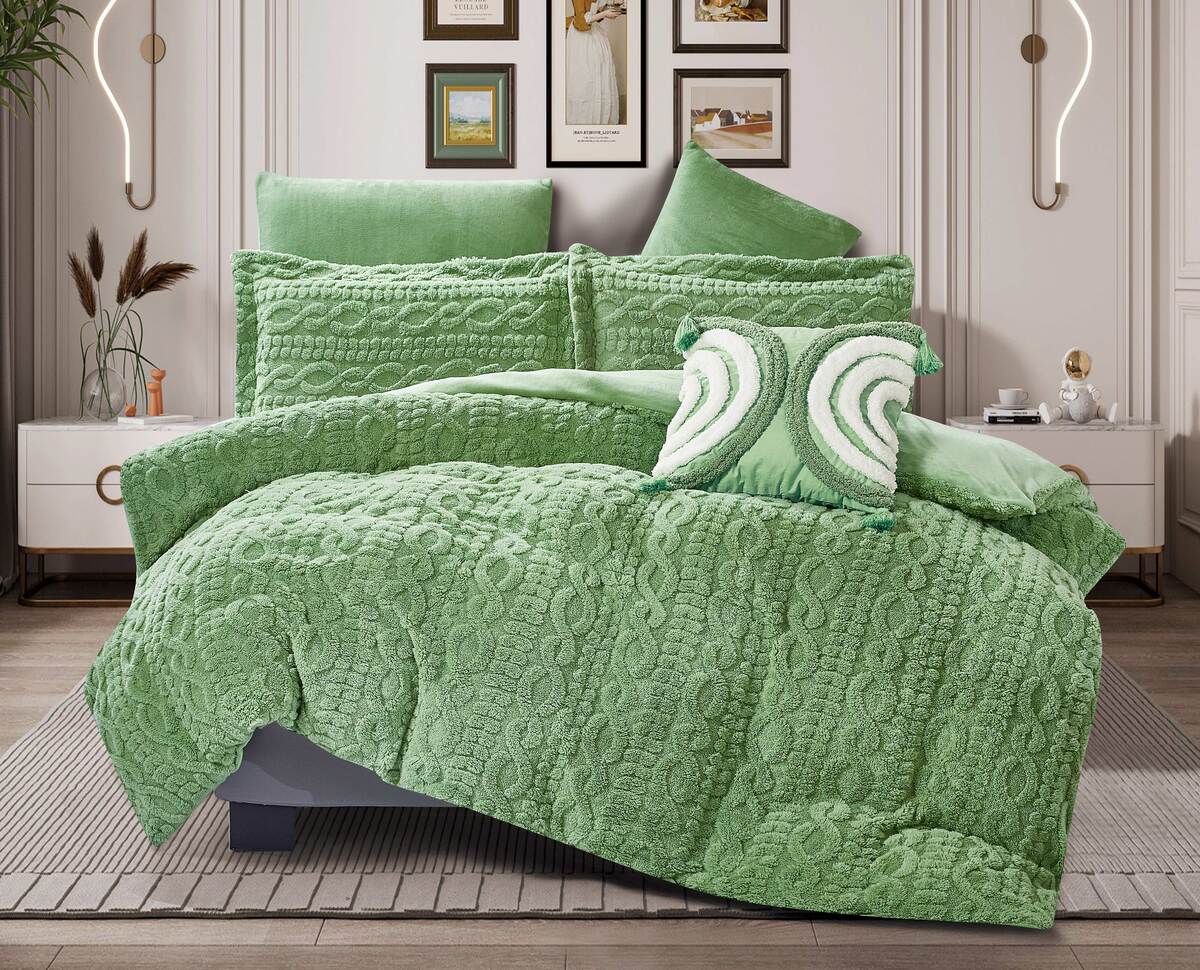 An emerald green quilted flannel comforter set on a bed, with additional pillows and a comforter draped over the edge of the bed, presented in a room setting.