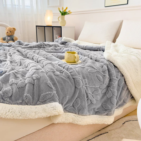 A gray solid sherpa throw with a floral pattern on a bed, with a white border. A teddy bear and a cup are visible on the bed.