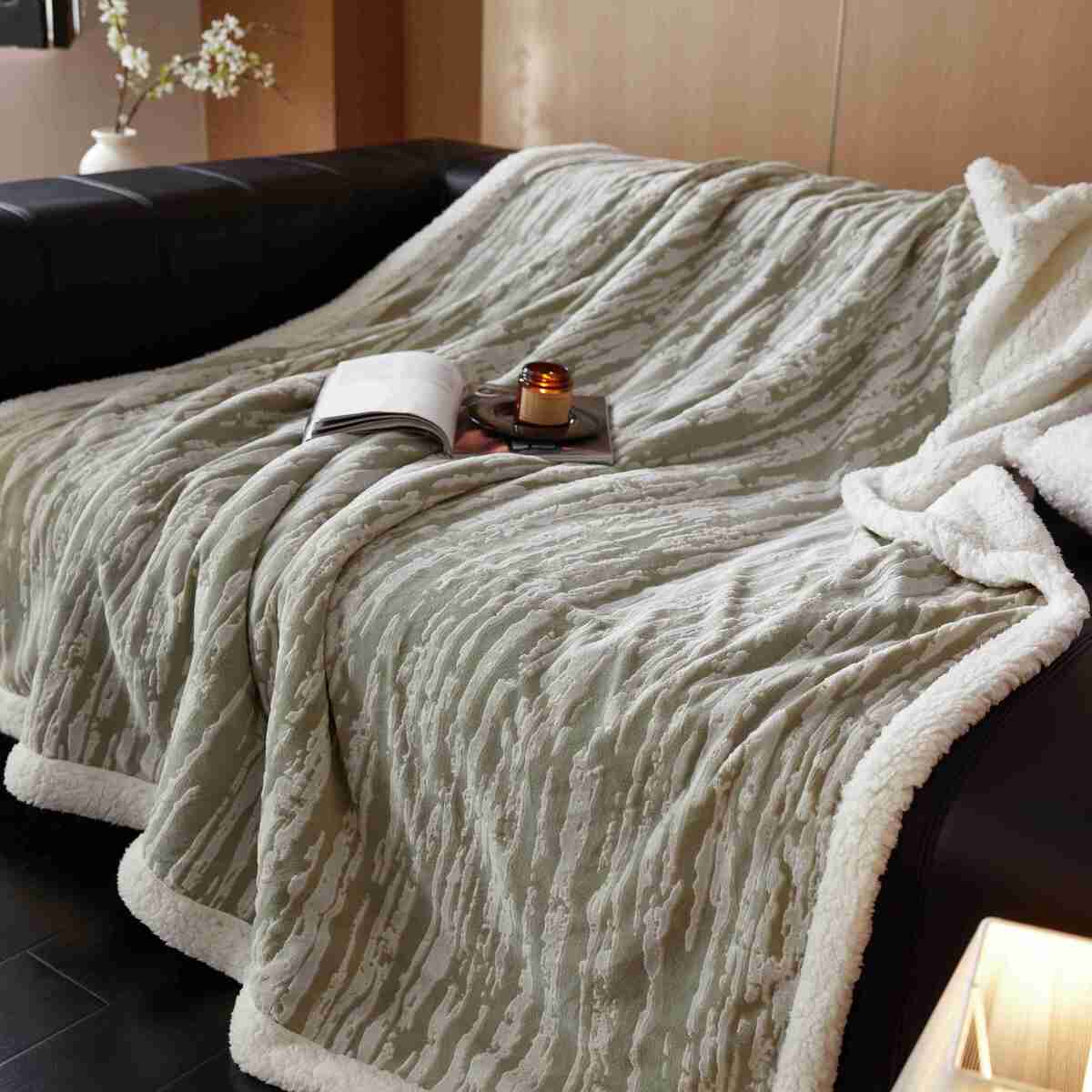 A beige Bohemian Fringe Sherpa Throw Blanket draped over the edge of a dark sofa, displaying its plush texture and fringe detailing.