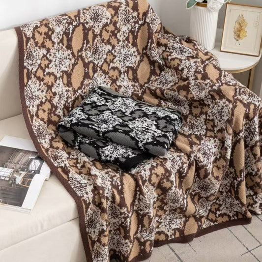 A brown, beige, and black hand-fringed throw with a geometric pattern draped over the back of a sofa.