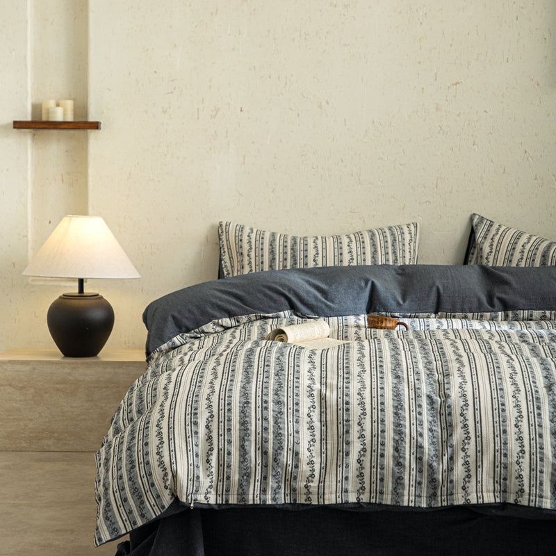 Bed with patterned bedding in a bedroom setting with a lamp and shelf.