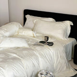 White satin bedding set on a bed with a black headboard.