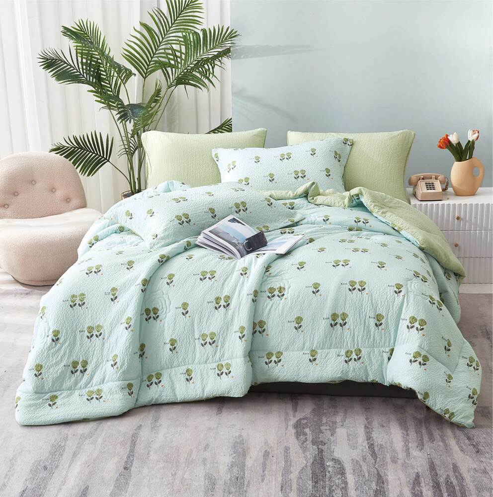 A green summer comforter set with a floral pattern displayed on a bed, accompanied by matching pillows and a book on the bed.
