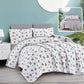 Floral bedding set on a bed with a nightstand and lamp in a room setting.