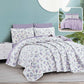 Floral bedding set with purple accents on a bed in a room with a light blue wall.