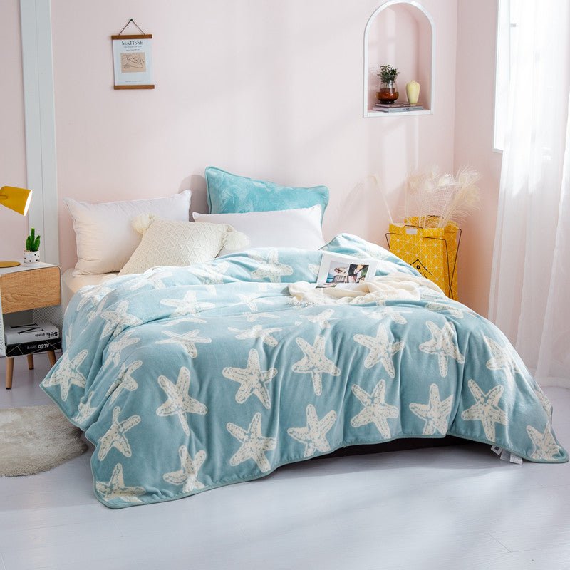 A blue fleece throw blanket with a white animal (starfish?) pattern spread out on a bed in a room with light decor.