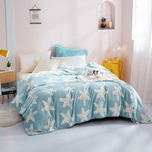 A blue fleece throw blanket with a white animal (starfish?) pattern spread out on a bed in a room with light decor.