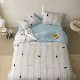 A bedding set with white and blue stripes and small animal (whale) patterns, displayed on a bed with pillows and a duvet cover.