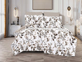 A bed with a white spread featuring a green and brown leaf print, displayed in a room with decorative lighting and a framed picture on the wall.