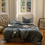 An ash grey summer bedding set on a bed, with a pillow, in a room with a window and wooden flooring.