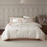A white duvet cover with embroidered corner details, displayed on a bed in a room with elegant wall paneling.