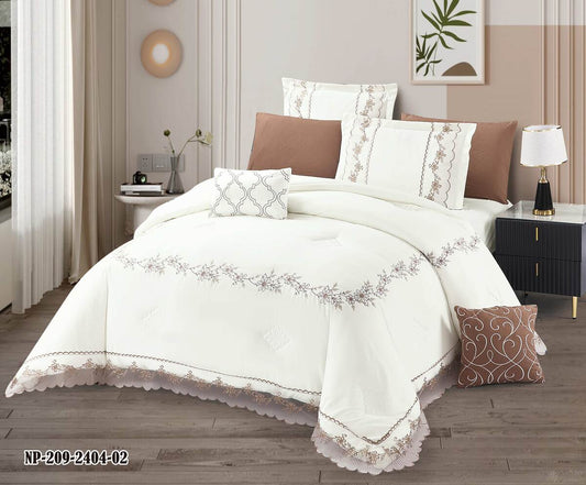 A white comforter set with floral lace detailing, displayed in a bedroom setting with brown accent pillows and a matching white and brown valance.