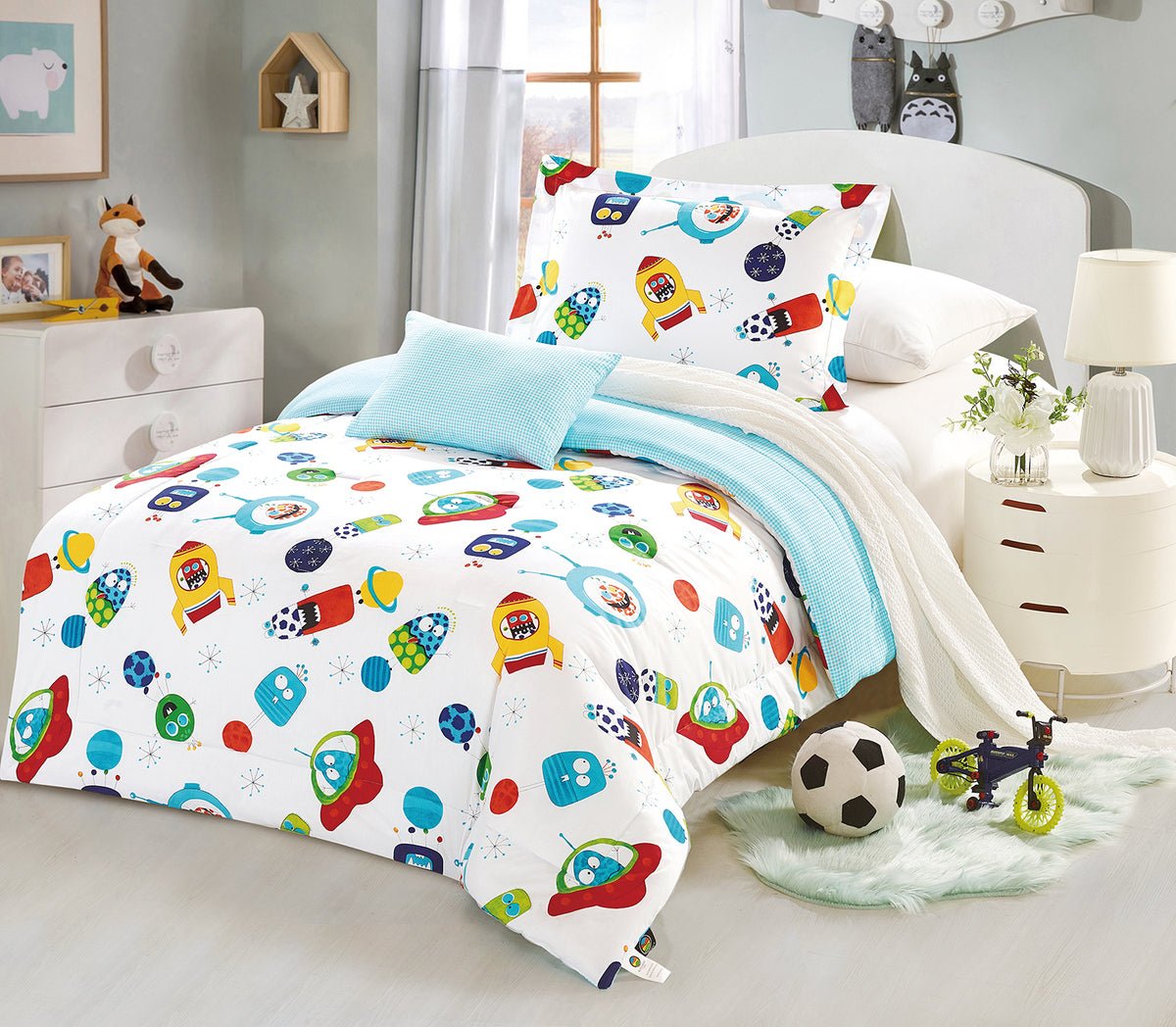 A bedding set with a space-themed print, featuring rockets and planets, displayed in a child's room.