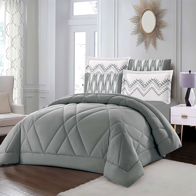 Gray quilted comforter set on a bed in a bedroom with decorative pillows and a lamp.