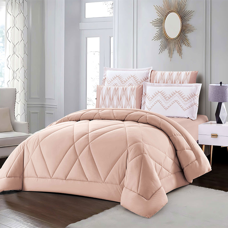 Bedroom with pink quilt and pillows on a bed, side table, and mirror.