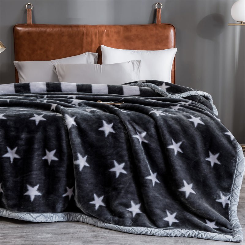 A gray and black Raschel fleece sofa blanket with star patterns, draped over a sofa with a brown leather headboard in the background.
