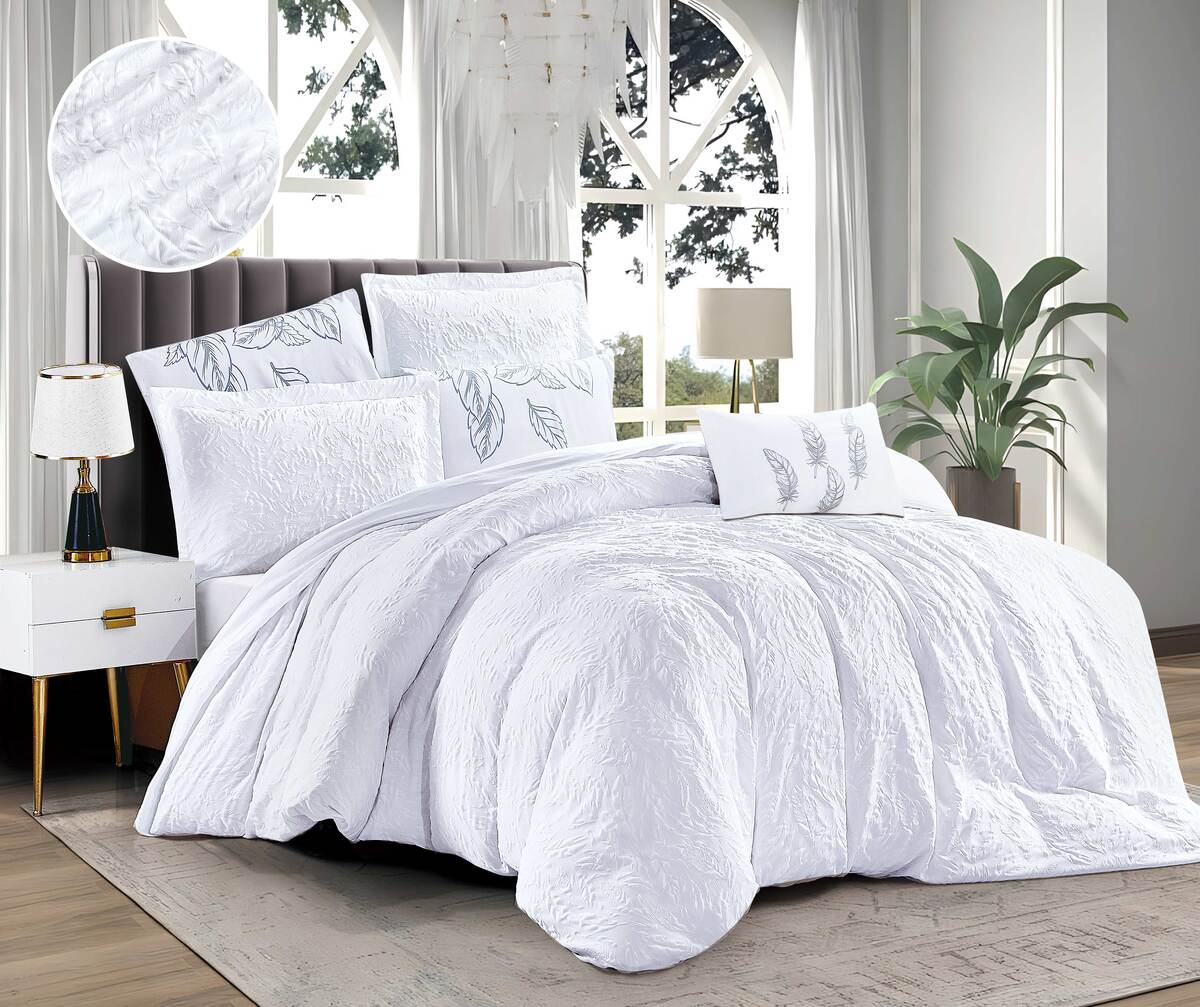 A white duvet cover with a floral print, displayed on a bed in a bedroom setting with a window, lamp, and plant in the background.