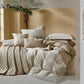 Neatly made bed with textured bedding and pillows in a room with a window and plant.